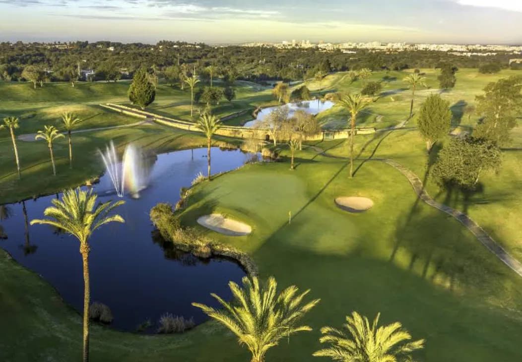 Aerial view of Gramacho Golf, with a lake and fountain framed by palm trees, greens and bunkers